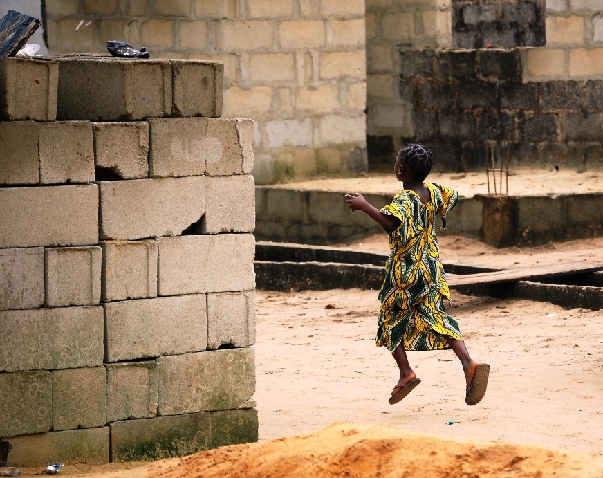 A little girl skips along through a construction site  which has sat uncompleted for a couple years. Concrete blocks are still a very integral material for building houses in Nigeria. Houses can take years to complete based on the current financial situation of their owners.
