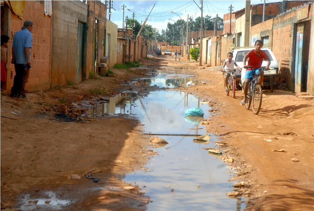 Image of a neighborhood with dirt streets and stagnant water with children riding bicycles.