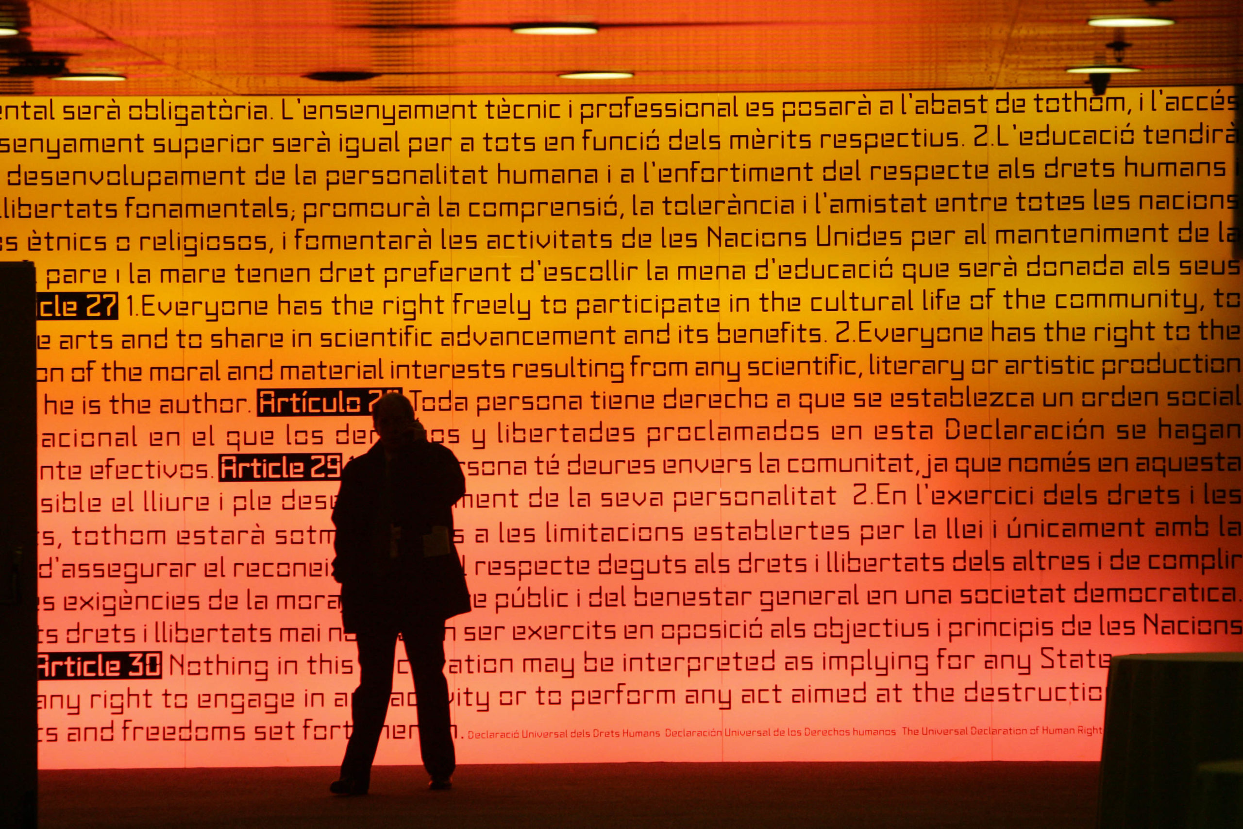 A man walks past an illuminated panel bearing the words of the Universal declaration of Human Rights at the international convention centre in Barcelona during the Euromed summit, 27 November 2005. European and Mediterranean-rim leaders gathered in Barcelona Sunday for a first-ever summit between the regions, but the absence of most Mideast chiefs clouded hopes of relaunching a 10-year-old partnership.AFP PHOTO/ADRIAN DENNIS (Photo by Adrian DENNIS / AFP)